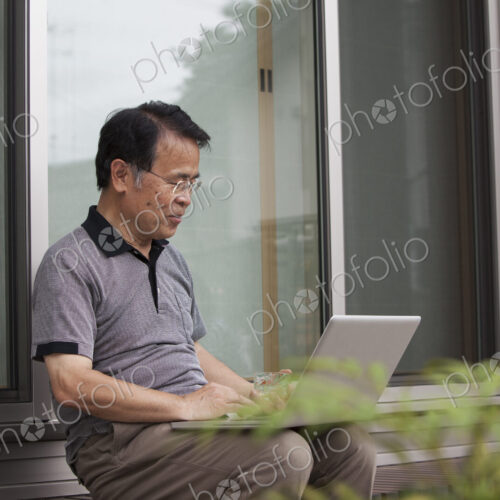 A man sitting outside a house. Holding a laptop computer.