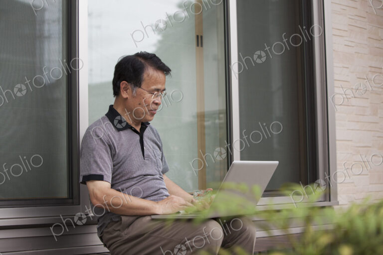A man sitting outside a house. Holding a laptop computer.