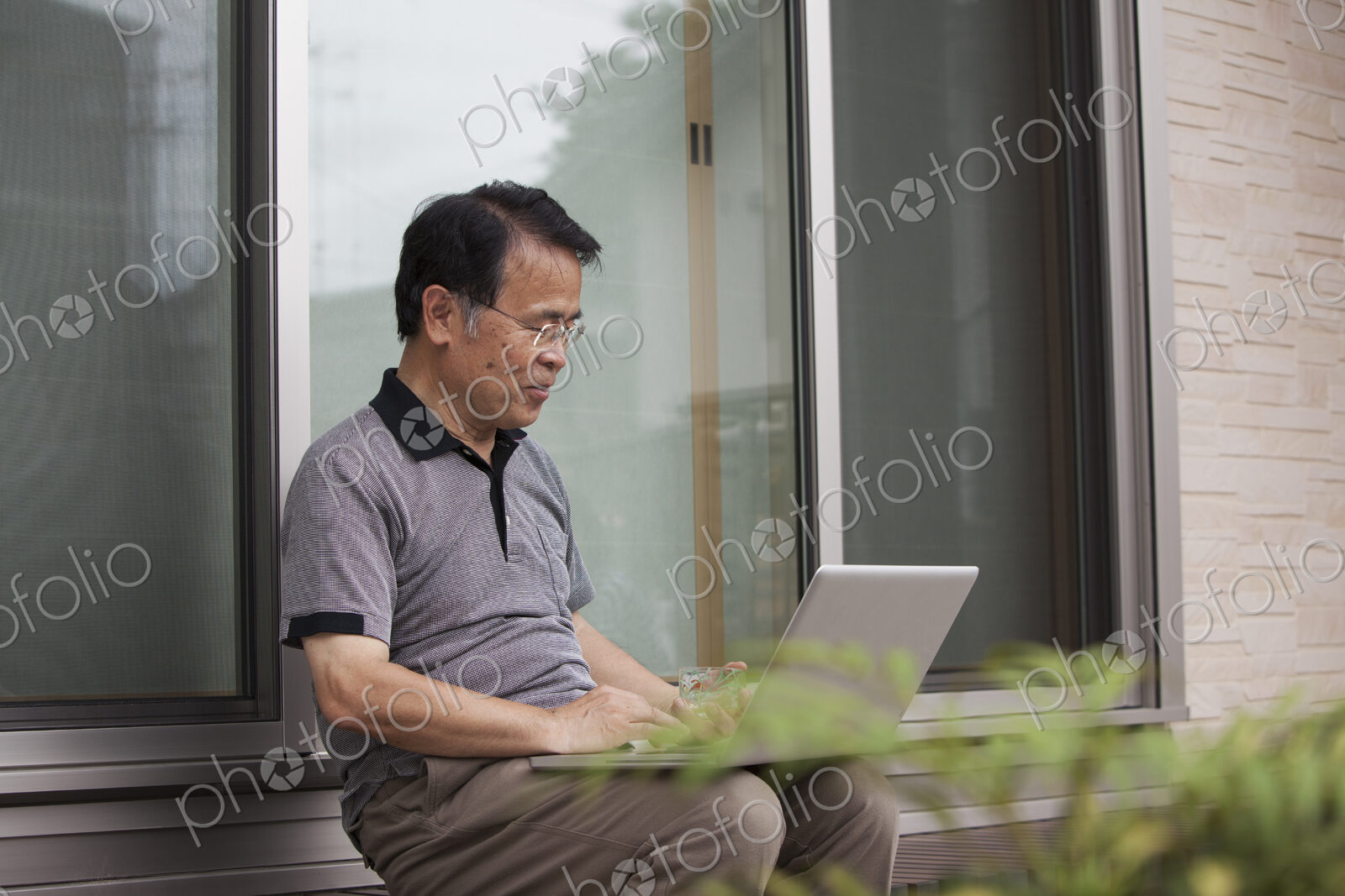 A man sitting outside a house. Holding a laptop computer.
