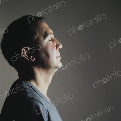 A man sitting still in repose eyes closed, light source shining on his face.