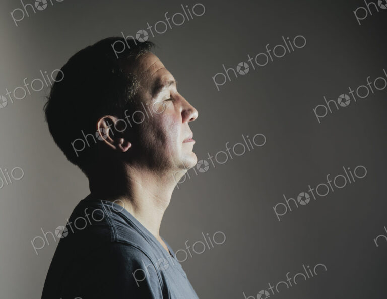 A man sitting still in repose eyes closed, light source shining on his face.