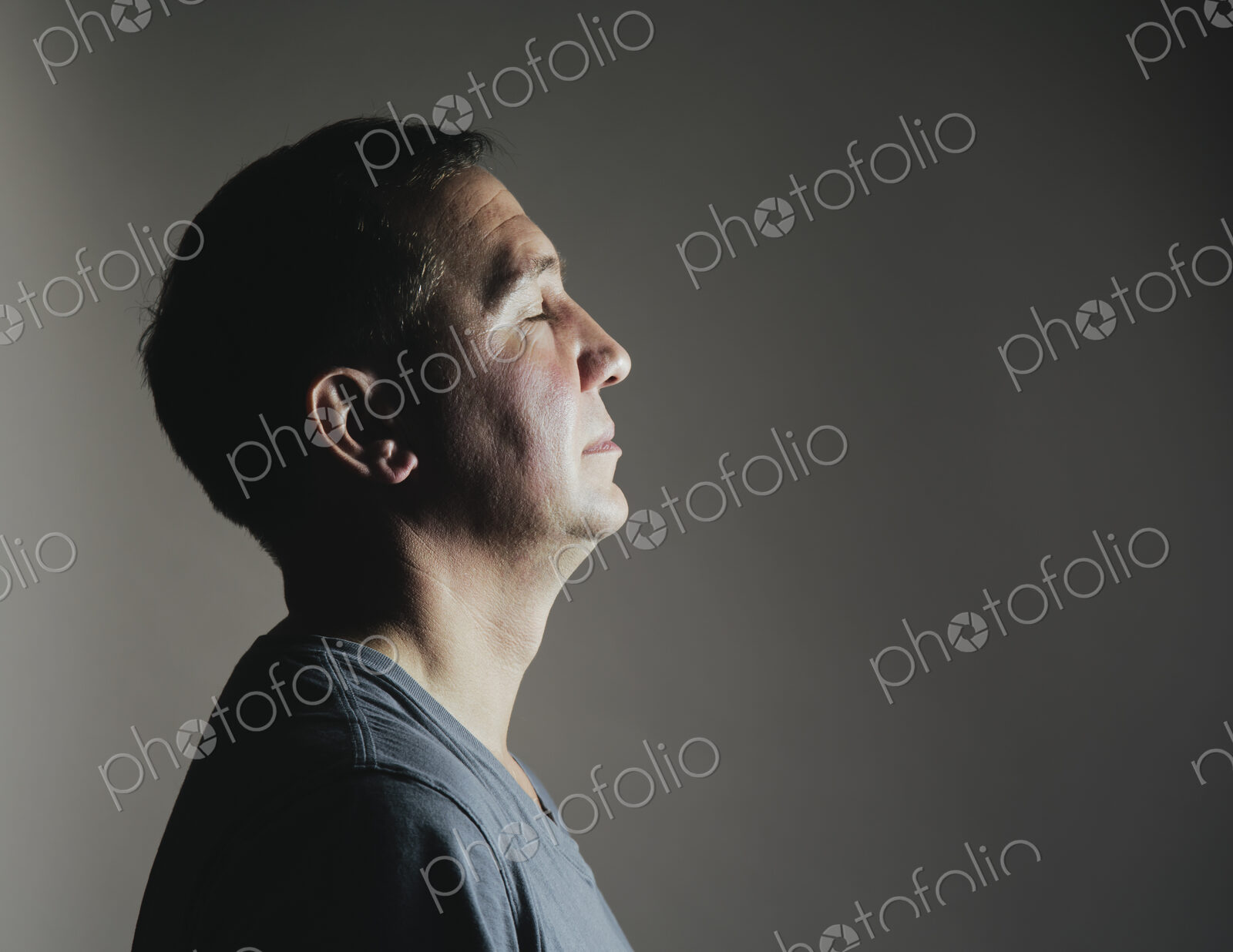 A man sitting still in repose eyes closed, light source shining on his face.
