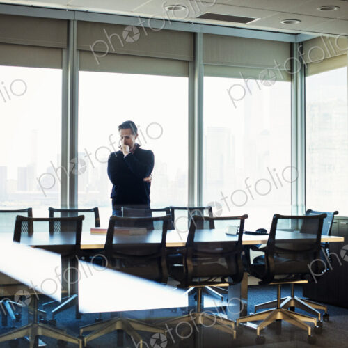 A man standing at a table in a meeting room looking down at an open book. A man standing at a table in a meeting room looking down at an open book.
