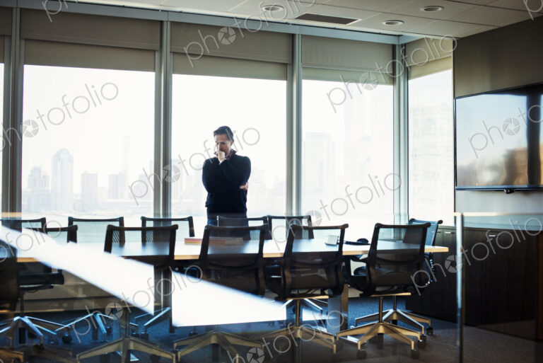 A man standing at a table in a meeting room looking down at an open book.