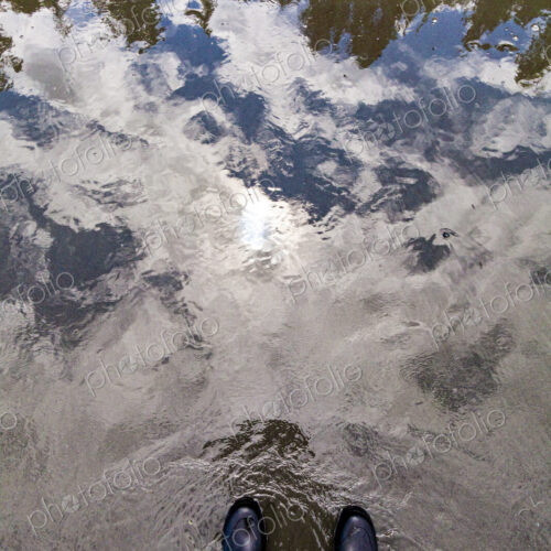 A man standing at the water's edge, a reflection of the forest and the sky in shallow… A man standing at the water's edge, a reflection of the forest and the sky in shallow…