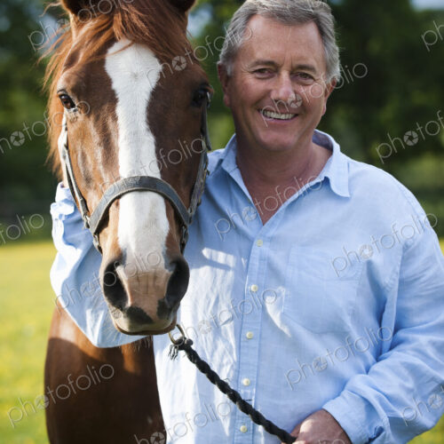A man standing holding the halter of a bay horse with a white flash on its muzzle. A man standing holding the halter of a bay horse with a white flash on its muzzle.