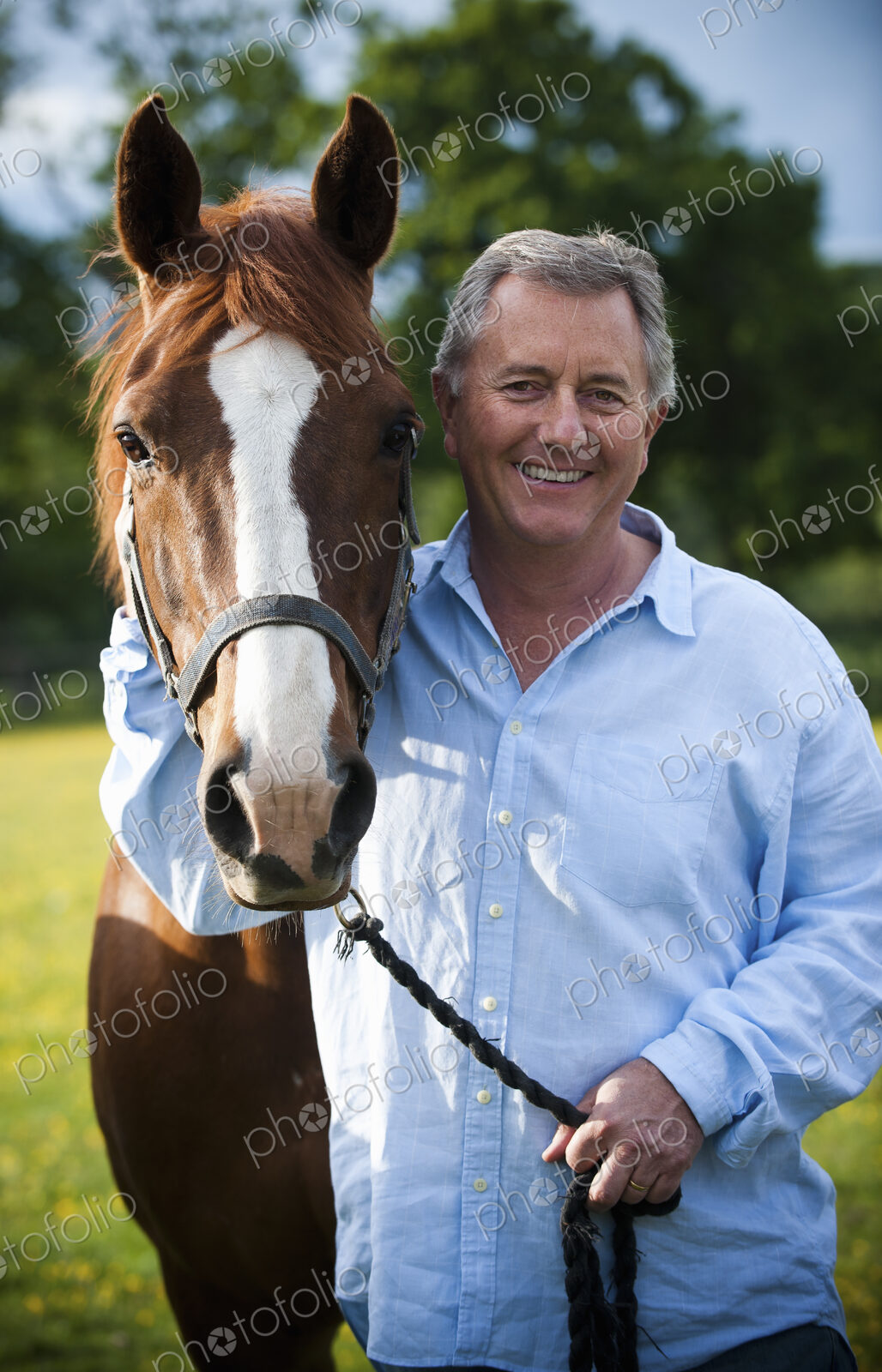 A man standing holding the halter of a bay horse with a white flash on its muzzle.