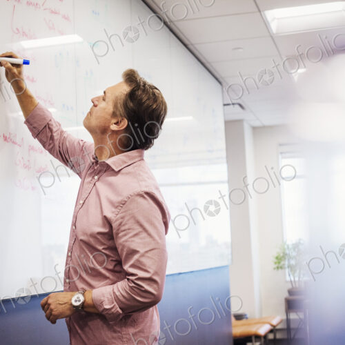 A man standing in a classroom writing on a whiteboard. A man standing in a classroom writing on a whiteboard.