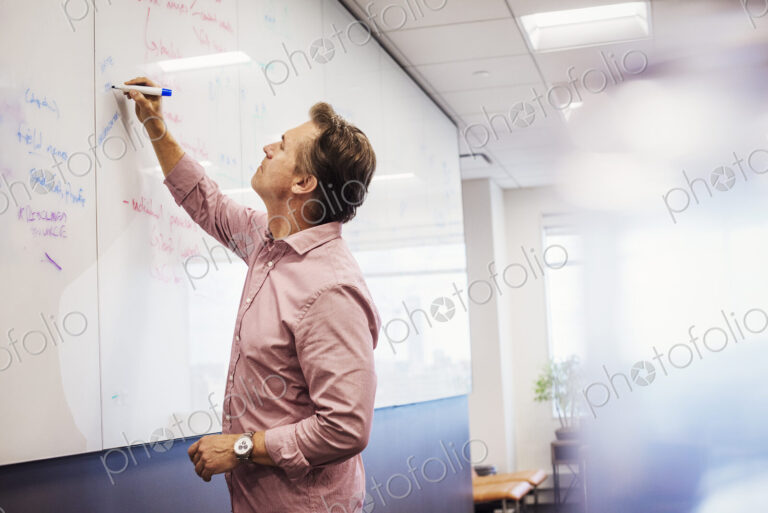 A man standing in a classroom writing on a whiteboard.