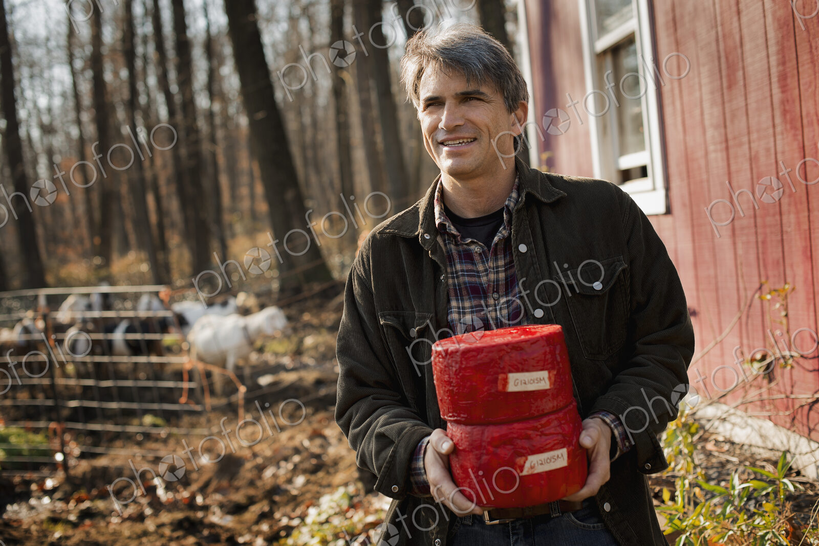 A man standing in a farm courtyard, holding two blocks of goat’s cheese.