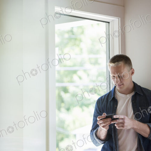 A man standing in a quiet corner of a cafe, using a smart phone. A man standing in a quiet corner of a cafe, using a smart phone.