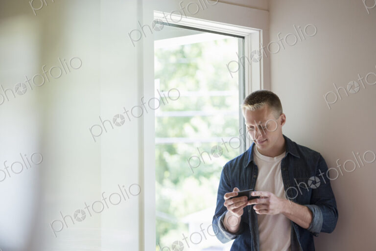 A man standing in a quiet corner of a cafe, using a smart phone.
