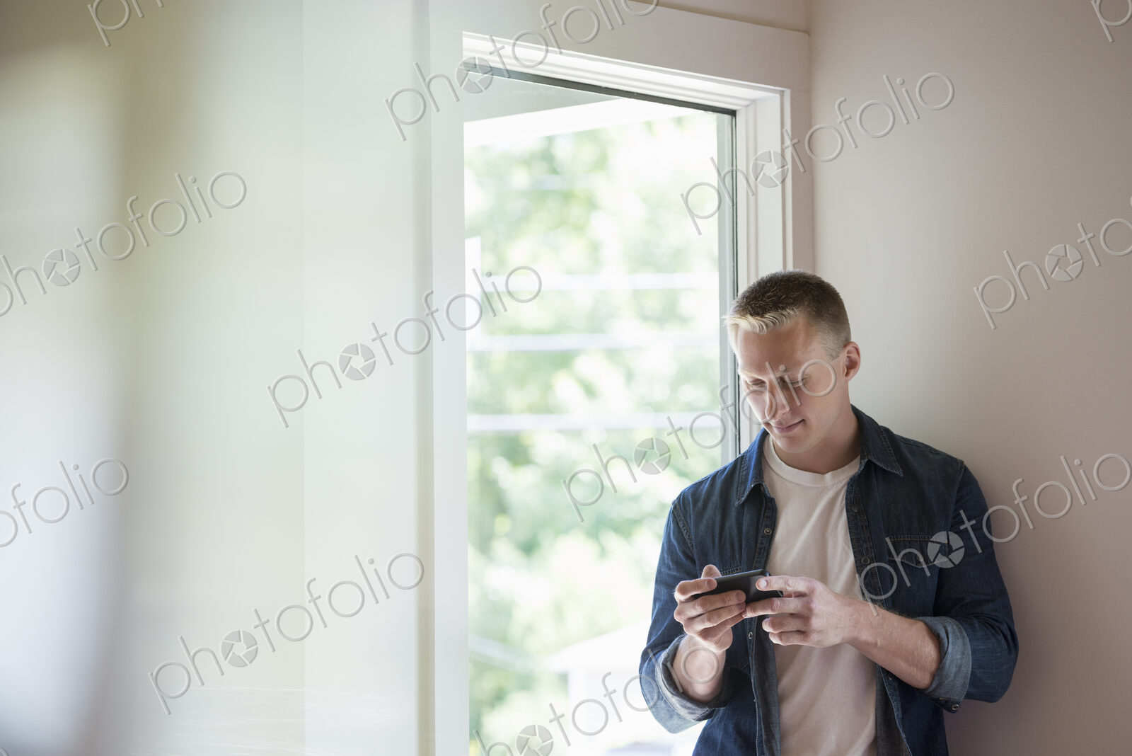 A man standing in a quiet corner of a cafe, using a smart phone.