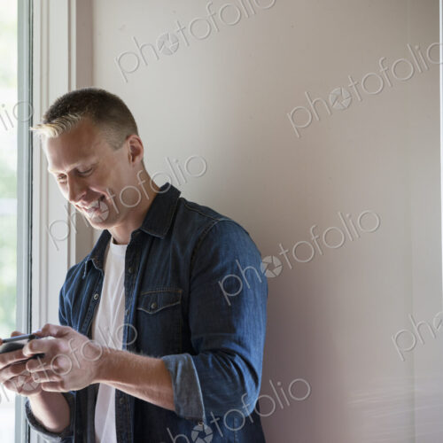 A man standing in a quiet corner of a cafe, using a smart phone. A man standing in a quiet corner of a cafe, using a smart phone.