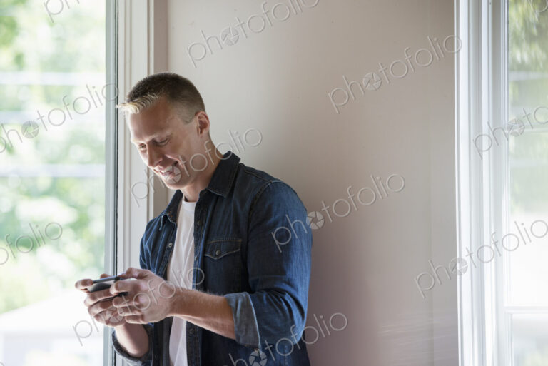 A man standing in a quiet corner of a cafe, using a smart phone.