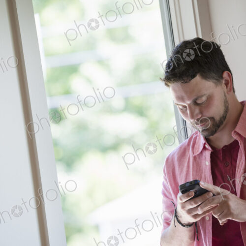 A man standing in a quiet corner of a cafe, using a smart phone. A man standing in a quiet corner of a cafe, using a smart phone.