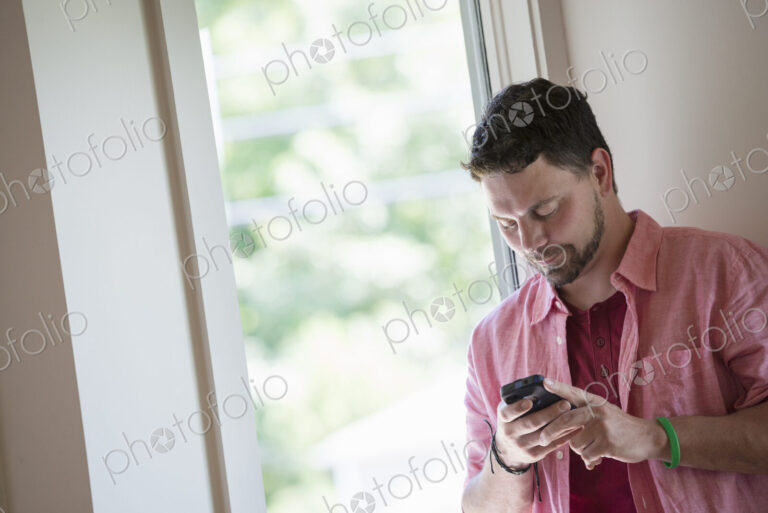 A man standing in a quiet corner of a cafe, using a smart phone.