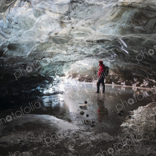 A man standing in an ice cave lit up with light, with clear contoured ice on the…