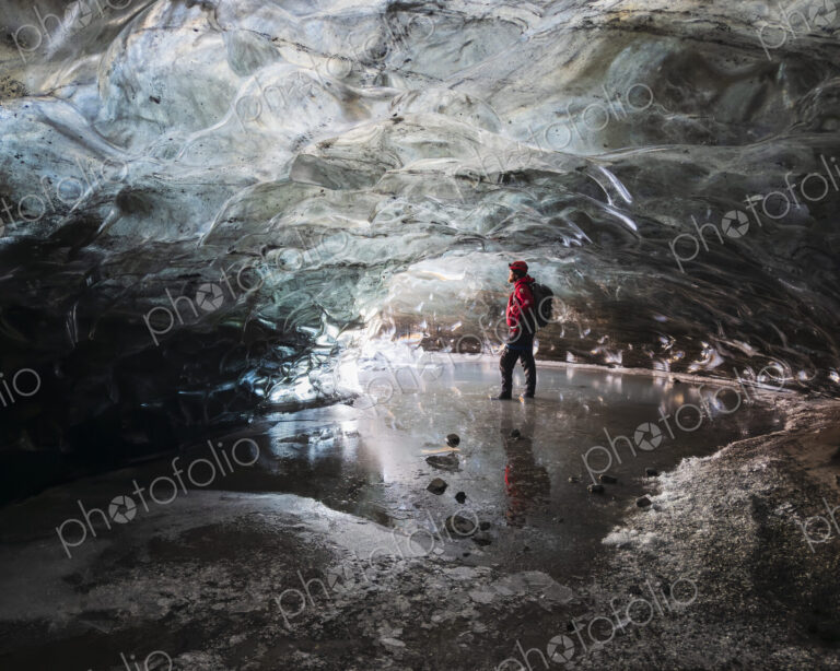 A man standing in an ice cave lit up with light, with clear contoured ice on the…