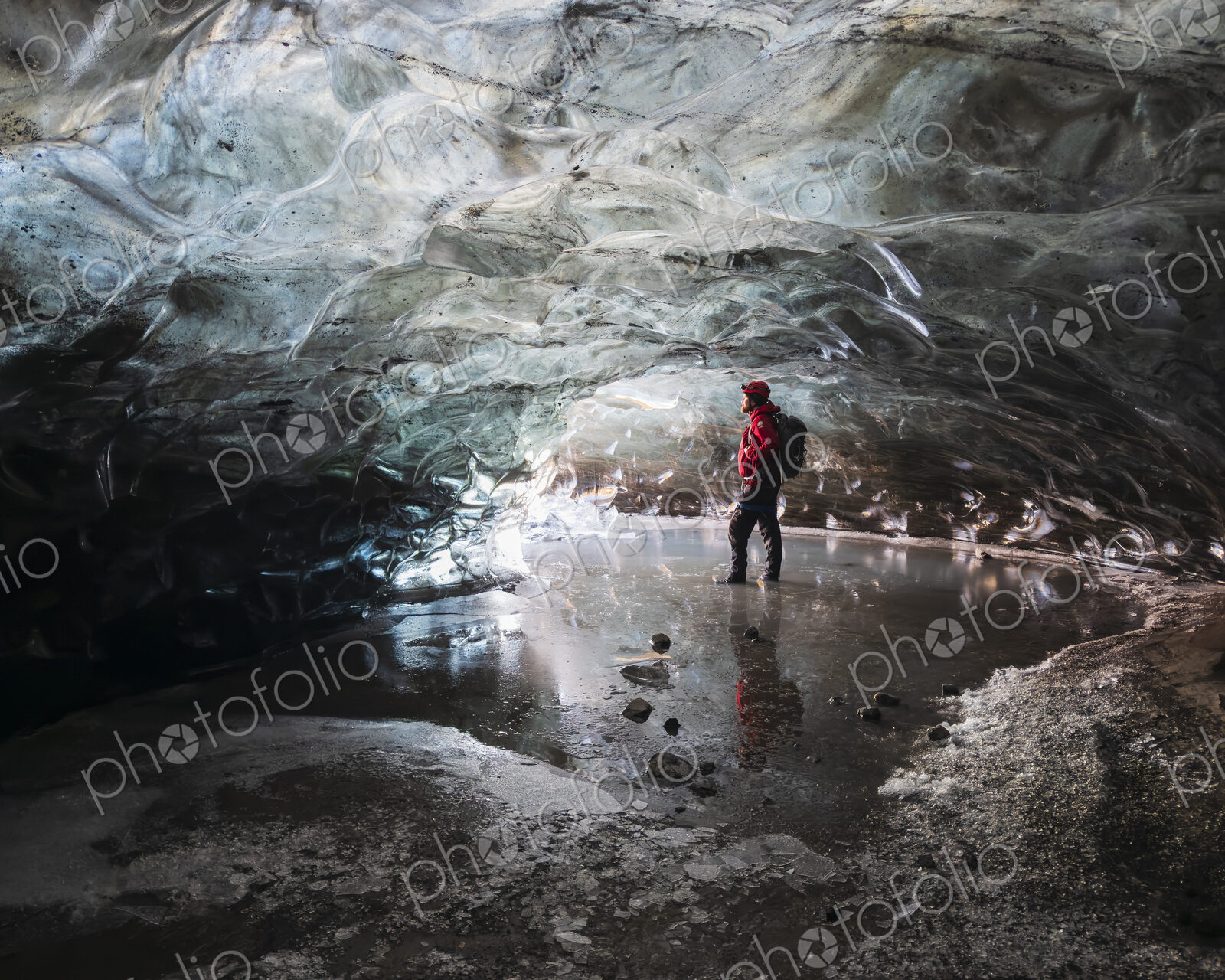 A man standing in an ice cave lit up with light, with clear contoured ice on the…