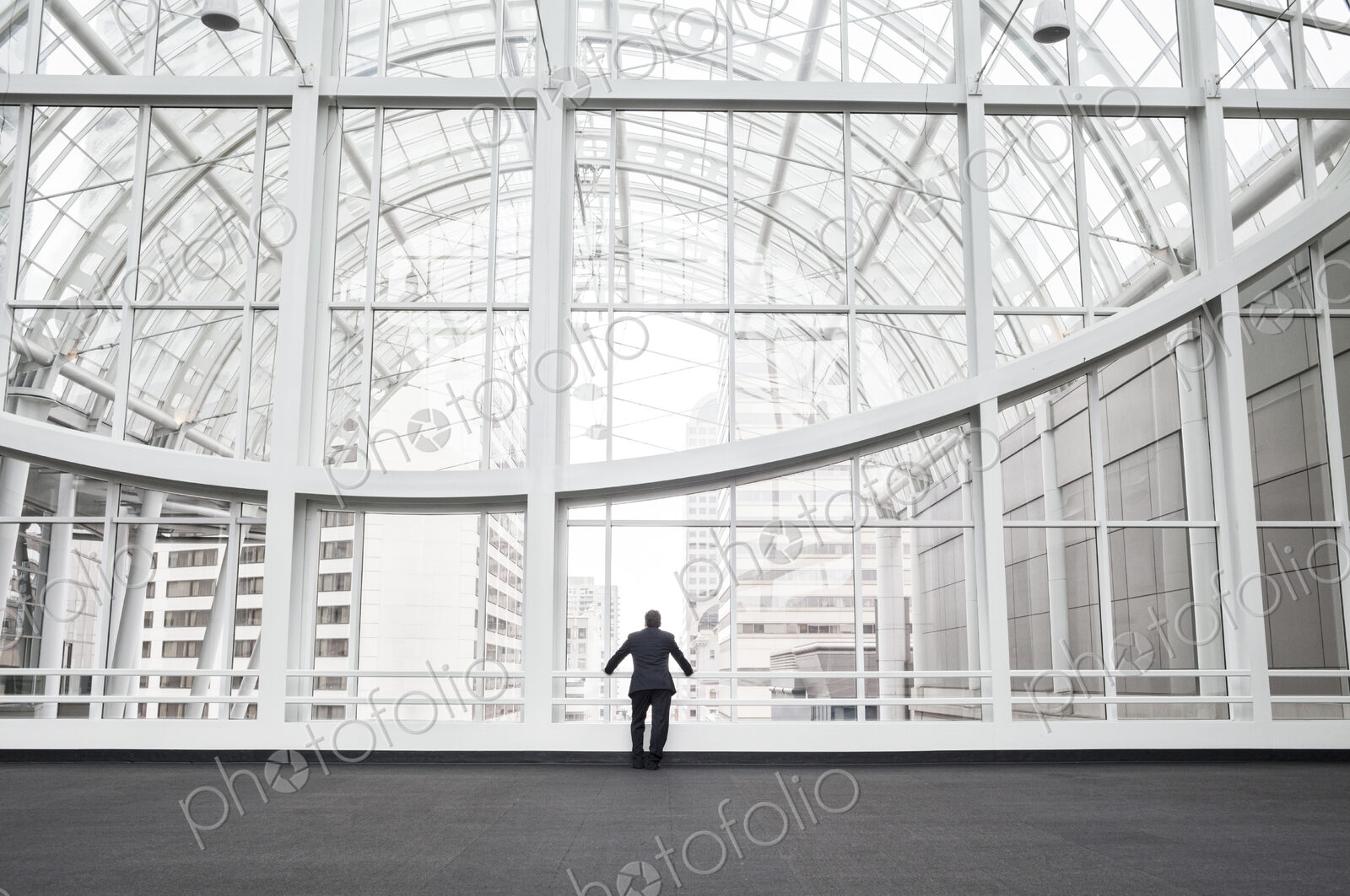 A man standing in an open space in a glass atrium in an office building, leaning on a…