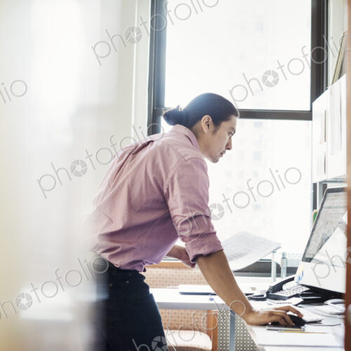 A man standing in his office leaning on the desk, viewed through an open door. A man standing in his office leaning on the desk, viewed through an open door.