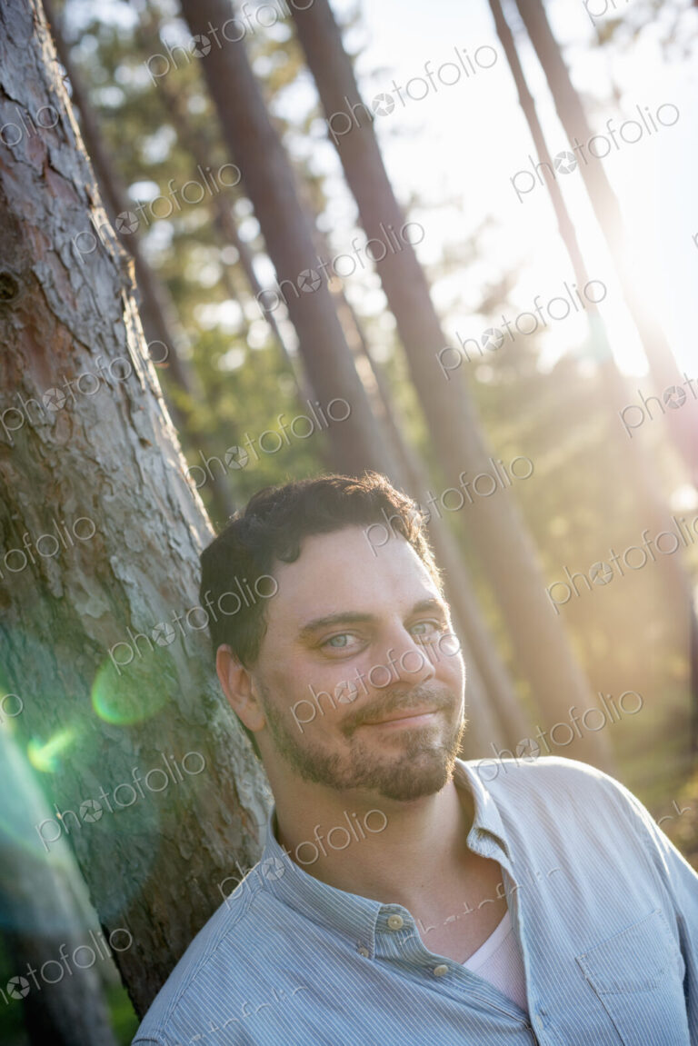 A man standing in woodland by a lake.