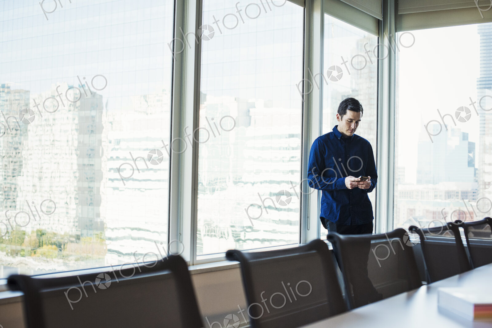 A man standing next to a table in a meeting room looking at a cellphone.