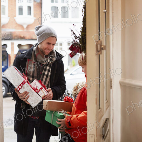 A man standing on a house doorstep with a stack of Christmas presents.