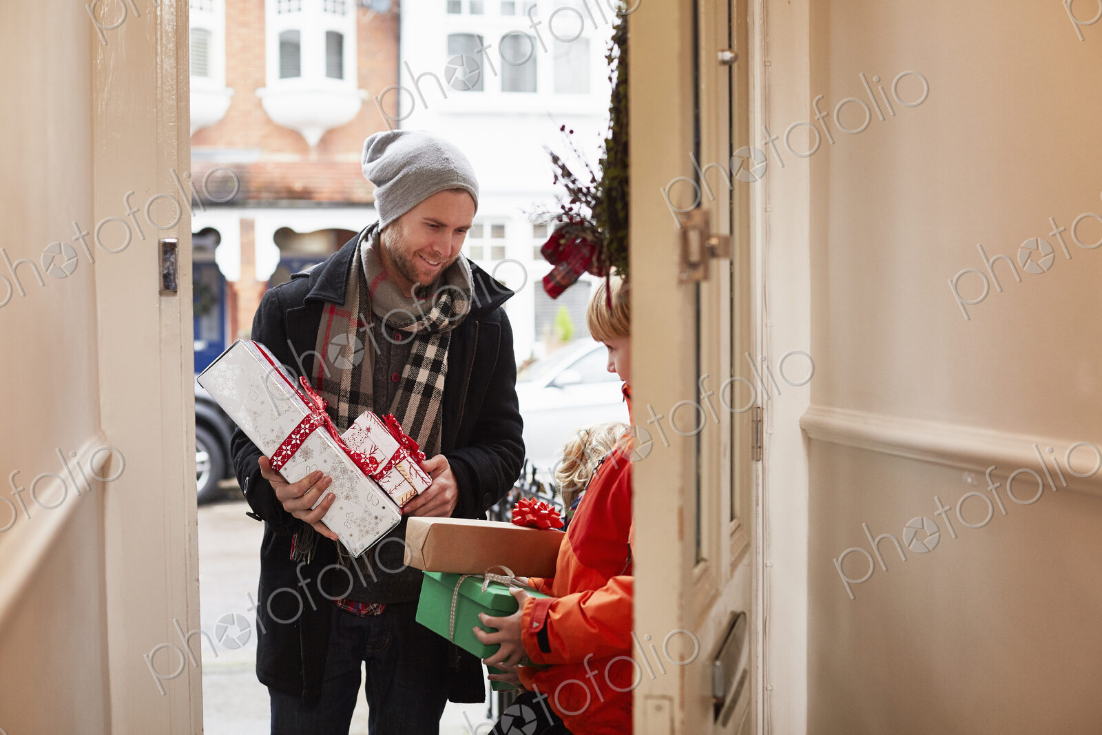 A man standing on a house doorstep with a stack of Christmas presents.