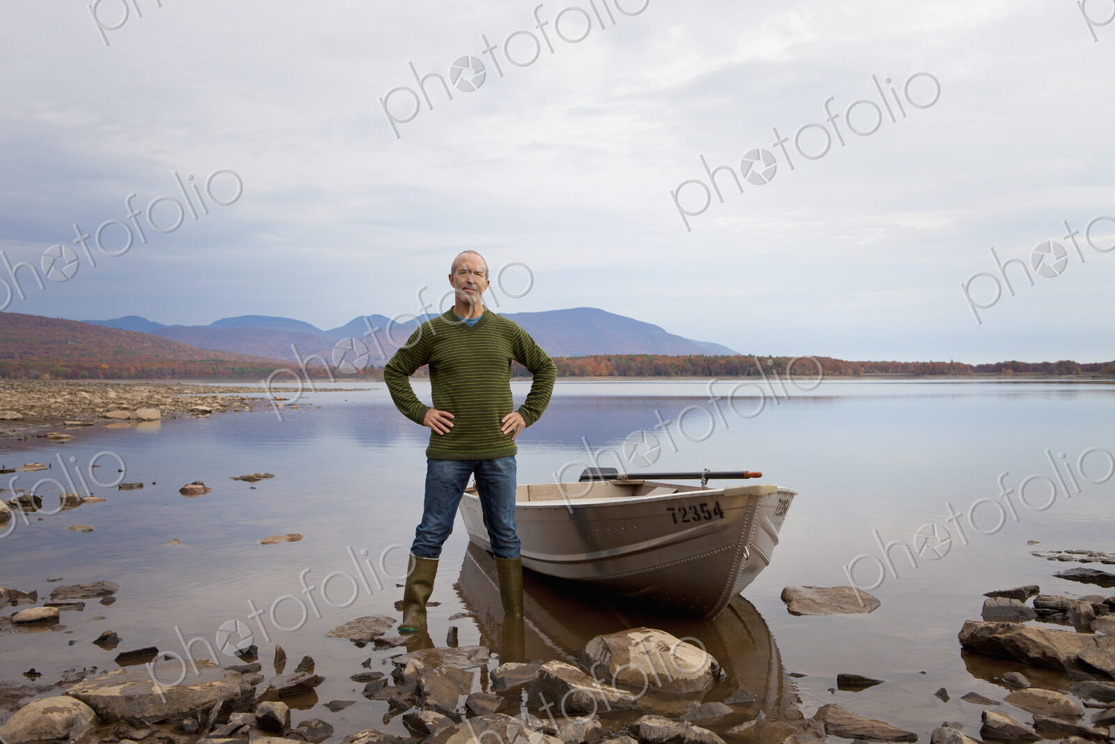 A man standing on a lake shore beside a small rowing boat.