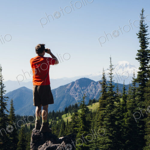 A man standing on a mountain ridge, taking a photograph of the landscape. A man standing on a mountain ridge, taking a photograph of the landscape.