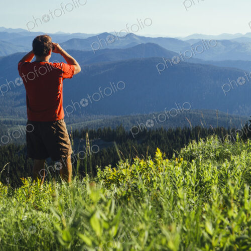 A man standing on a mountain ridge, taking a photograph of the landscape and forested… A man standing on a mountain ridge, taking a photograph of the landscape and forested…