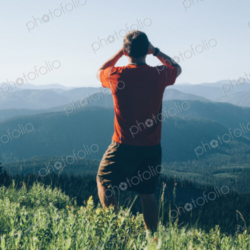 A man standing on a mountain ridge, taking a photograph of the landscape and forested… A man standing on a mountain ridge, taking a photograph of the landscape and forested…