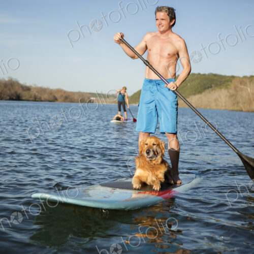 A man standing on a paddleboard with a dog.