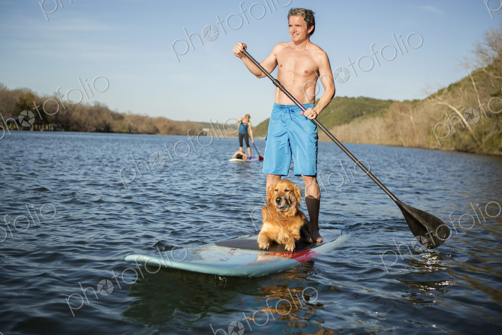 A man standing on a paddleboard with a dog.