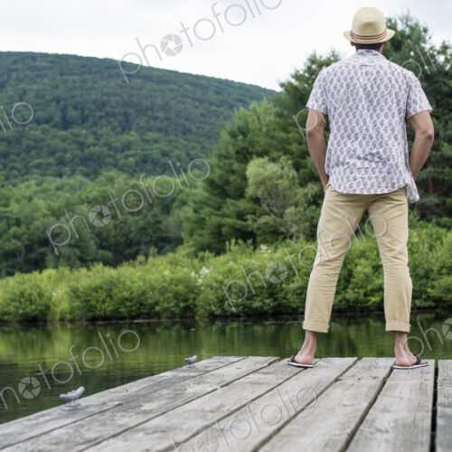 A man standing on a wooden pier overlooking a calm lake. A man standing on a wooden pier overlooking a calm lake.