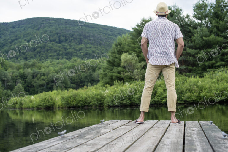A man standing on a wooden pier overlooking a calm lake.