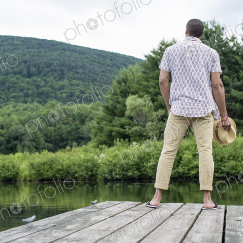 A man standing on a wooden pier overlooking a calm lake. A man standing on a wooden pier overlooking a calm lake.