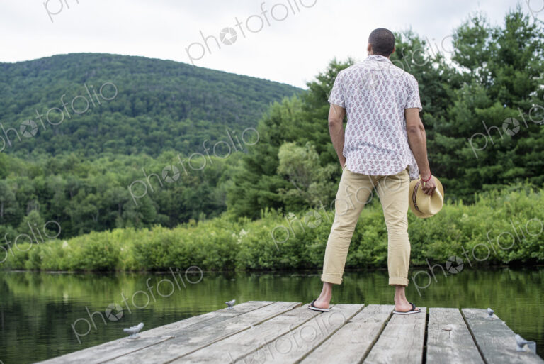 A man standing on a wooden pier overlooking a calm lake.