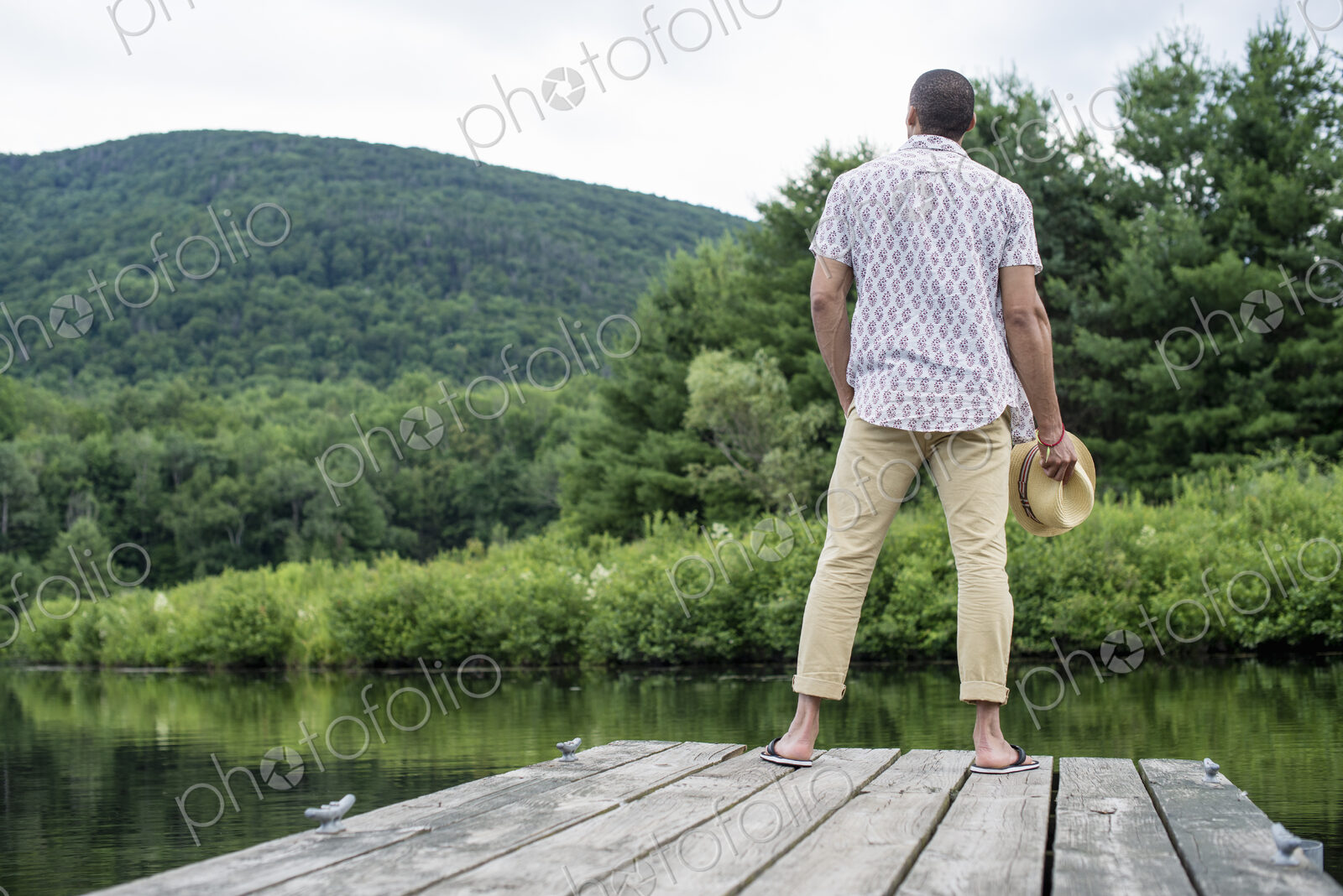 A man standing on a wooden pier overlooking a calm lake.