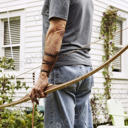 A man standing outdoors hoping a bow in his hand. A man standing outdoors hoping a bow in his hand.