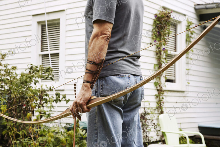 A man standing outdoors hoping a bow in his hand.