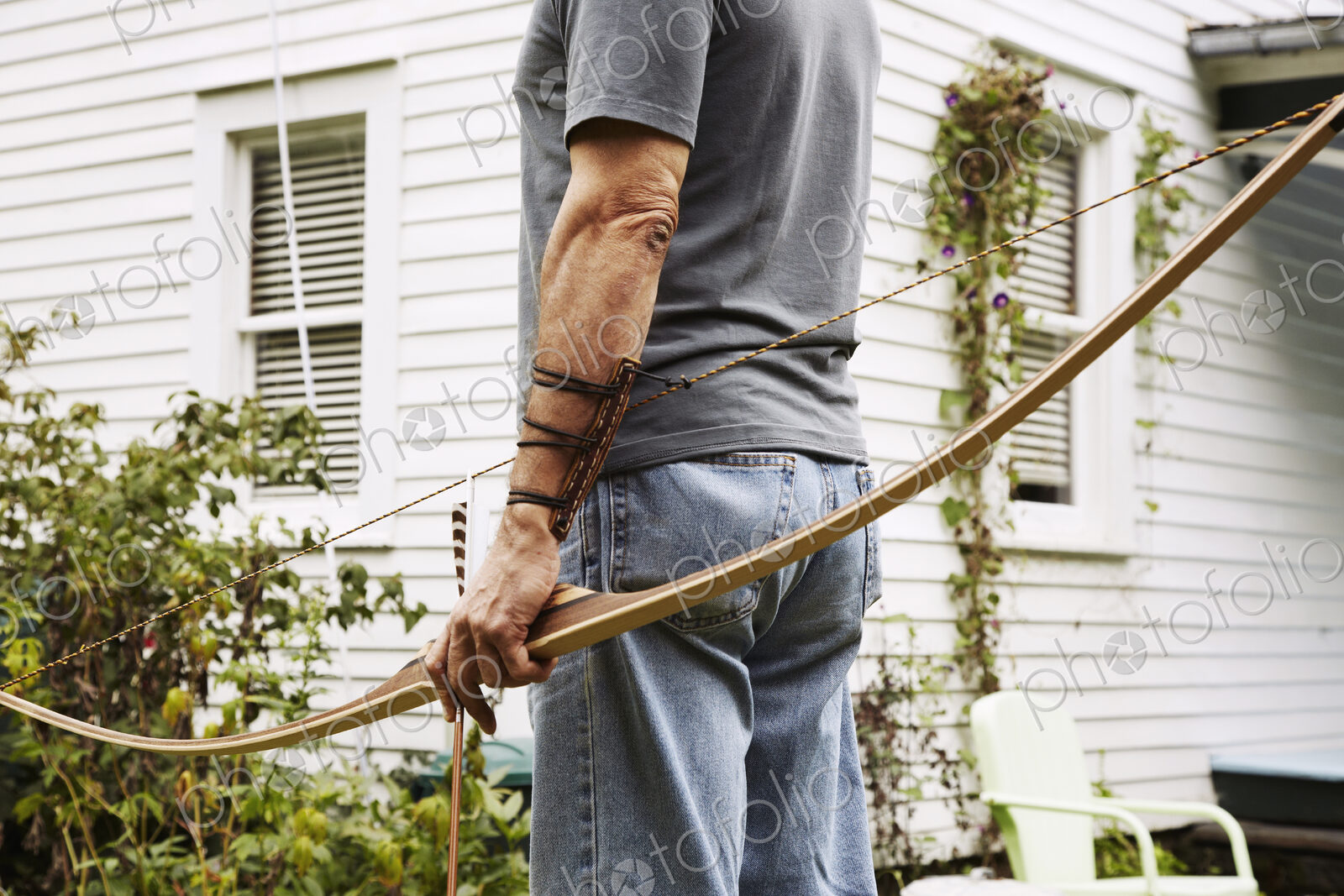 A man standing outdoors hoping a bow in his hand.