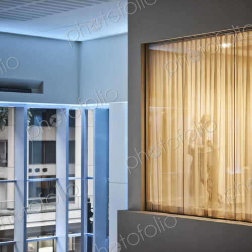 A man standing using h is phone in an office viewed from a building atrium. A man standing using h is phone in an office viewed from a building atrium.