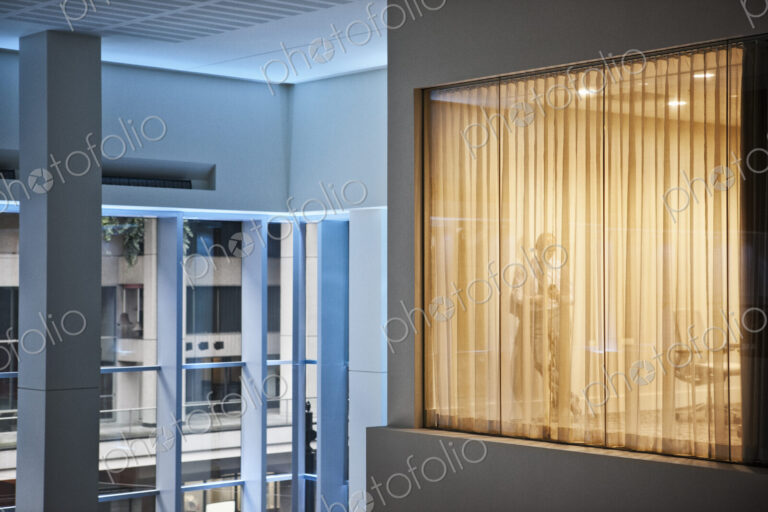 A man standing using h is phone in an office viewed from a building atrium.