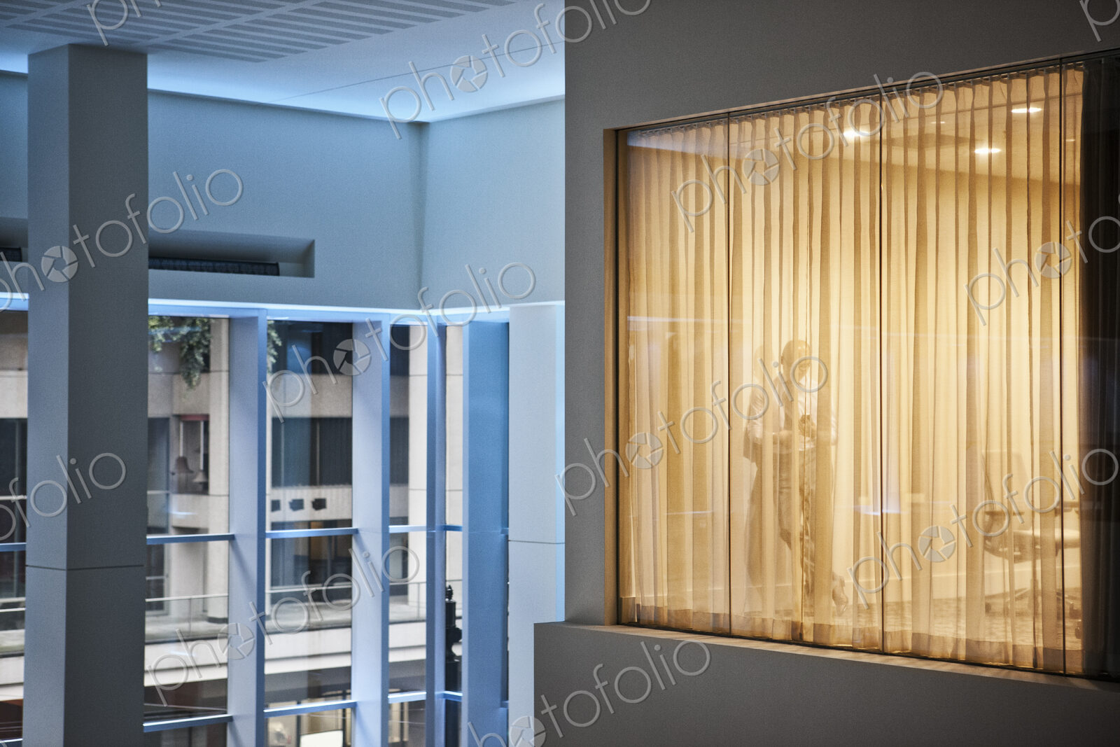 A man standing using h is phone in an office viewed from a building atrium.