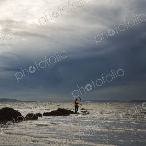 A man stands on a rock in the middle of the Puget Sound with his sea kayak floating… A man stands on a rock in the middle of the Puget Sound with his sea kayak floating…