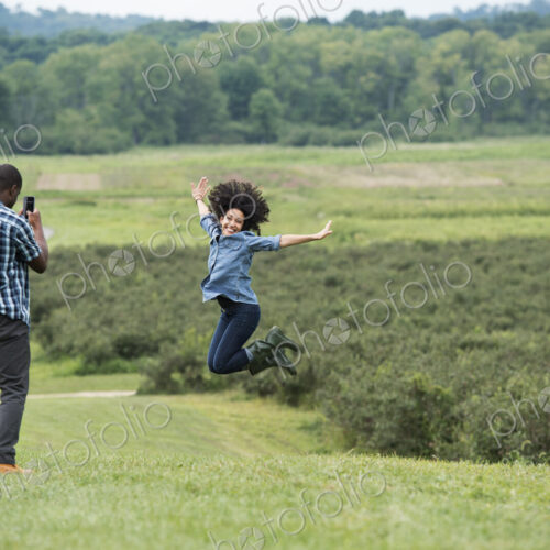 A man taking a photograph of a woman leaping in the air, jumping for joy with her arms… A man taking a photograph of a woman leaping in the air, jumping for joy with her arms…