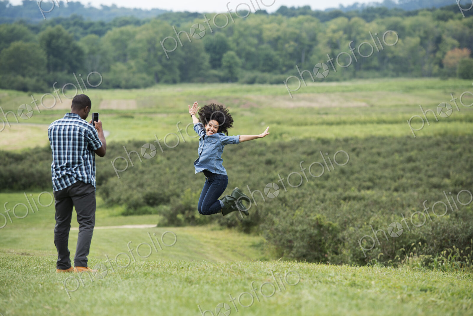A man taking a photograph of a woman leaping in the air, jumping for joy with her arms…